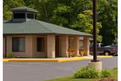 Single-story brick building entrance with a covered porte-cochere, potted plants, parked cars, and trees in the background.