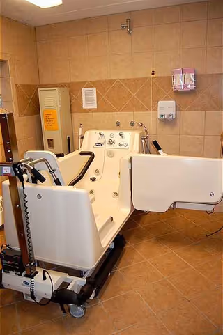 A patient lift chair is positioned beside a bathtub in a tiled bathroom.