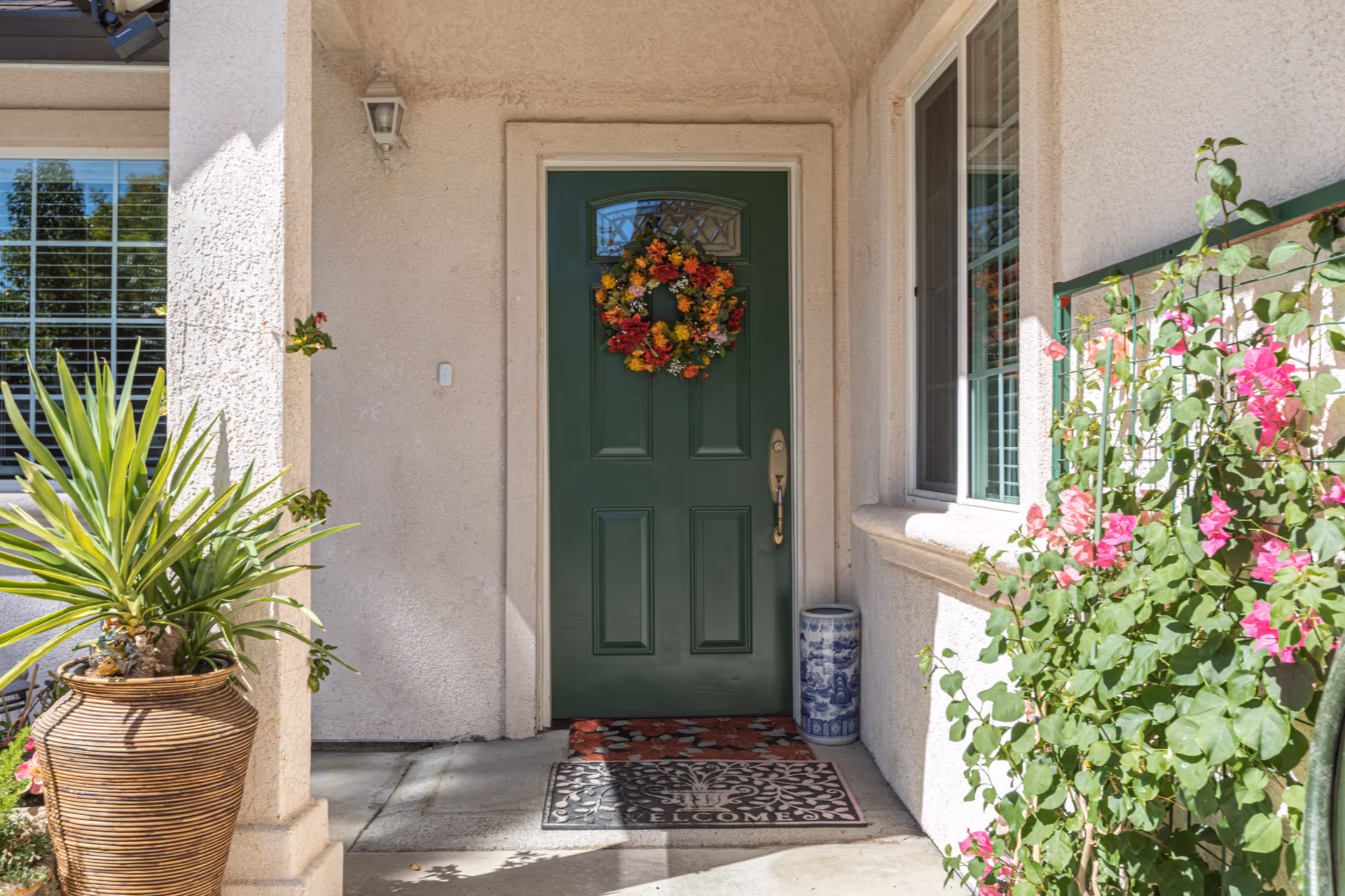 Front entrance with a green door adorned with a floral wreath, potted plants, and a welcome mat.