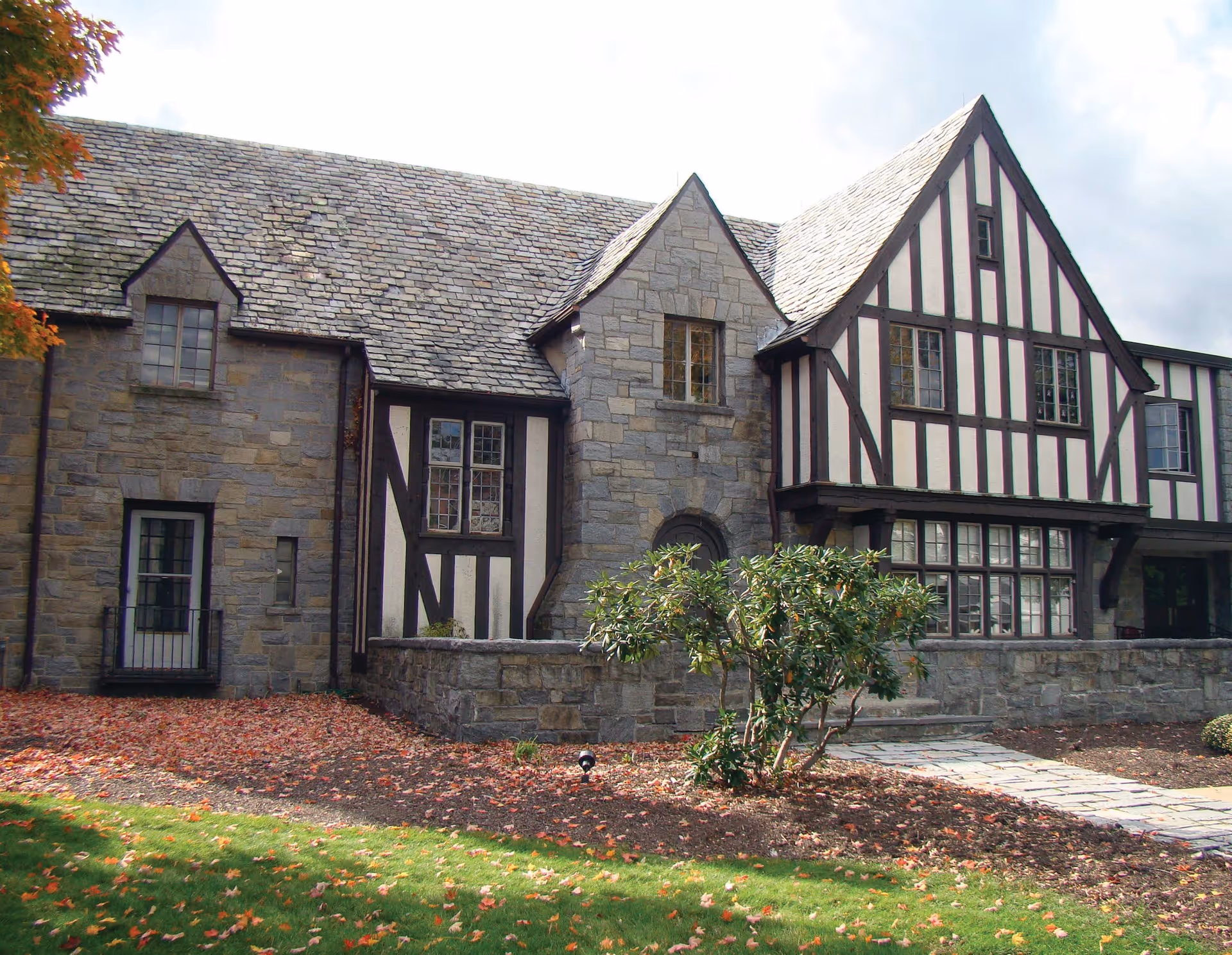 Exterior view of a stone and timber-framed building with a slate roof, surrounded by a lawn and some autumn leaves on the ground.
