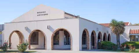Mission Arch Center exterior with arches, white walls, and a palm tree.