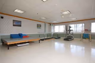 An empty rehabilitation room with a treadmill and therapy equipment.