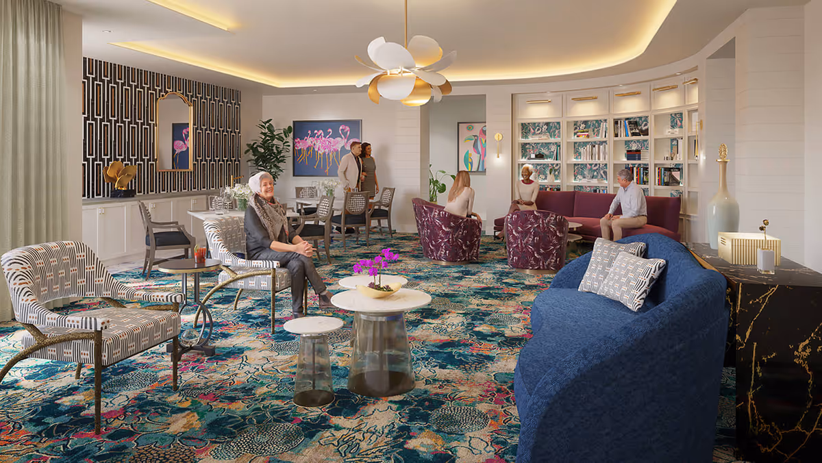 Bright, modern communal lounge with patterned carpet, multiple seating areas, bookshelves and several residents conversing.