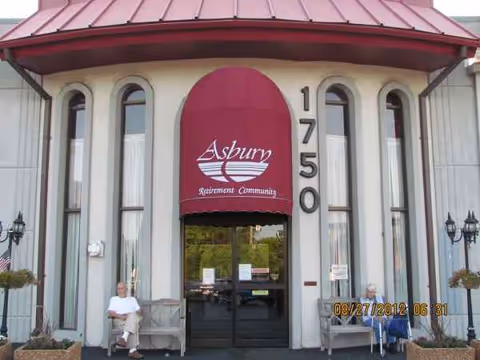 Exterior view of Asbury Court entrance with a red canopy and residents seated outside.