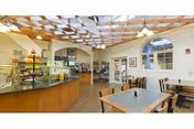 Bright dining room with tables and chairs, a curved service counter, decorative wooden trellis ceiling, and an arched window.