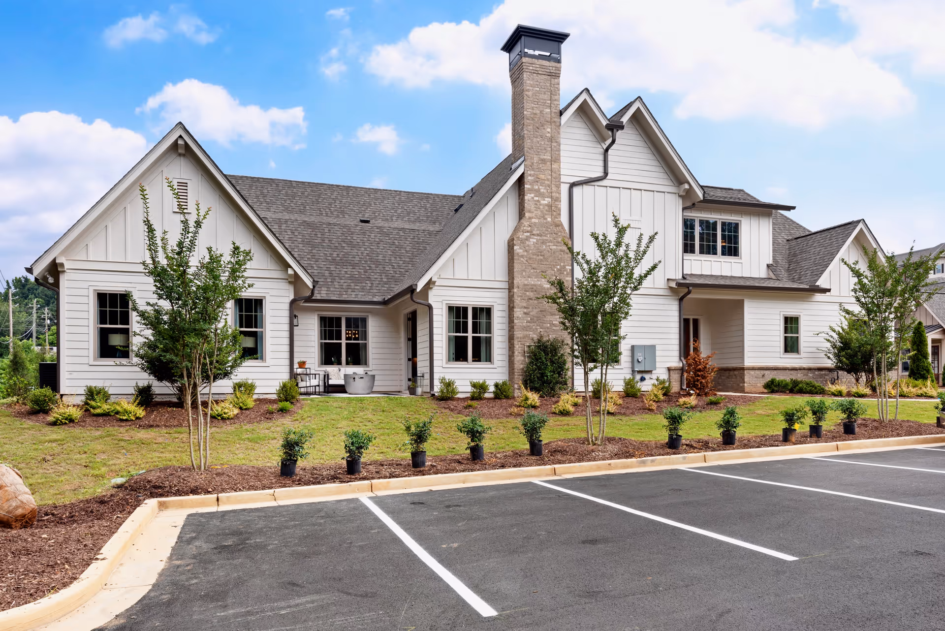 Front exterior of a modern white two-story residential building with a chimney, landscaped yard, and empty parking spaces.