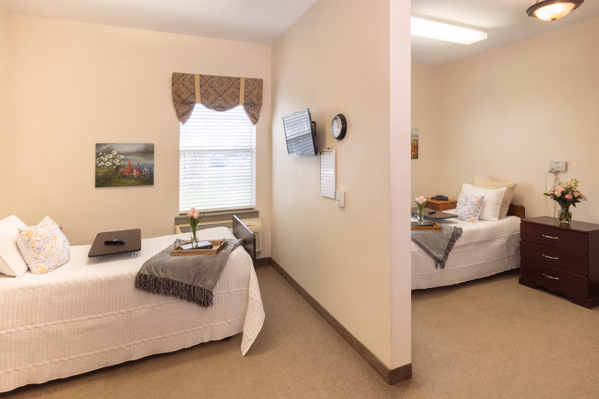 Shared bedroom with two single beds separated by a partial partition, each with bedside tables, flowers and soft decor.