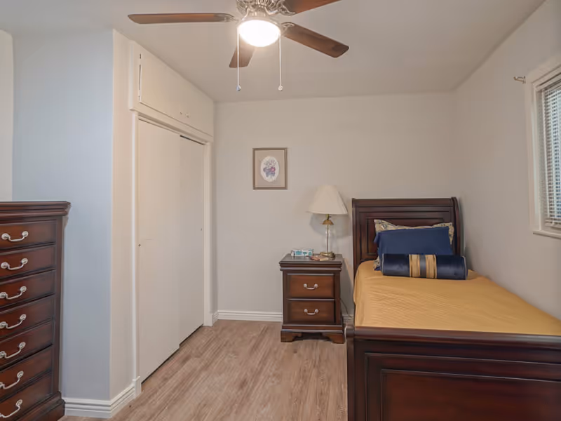 Single bedroom with a wooden twin bed, nightstand and dresser under a ceiling fan.