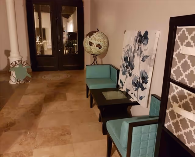 Lobby seating area with turquoise chairs and small tables, a decorative globe and floral artwork leaning against the wall near glass double doors.