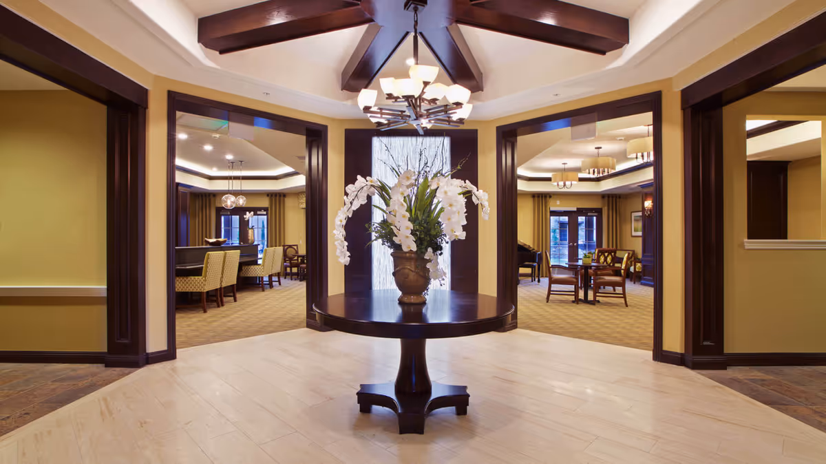 Elegant senior living lobby with a round table topped by a vase of white orchids and views into adjoining dining and seating areas.