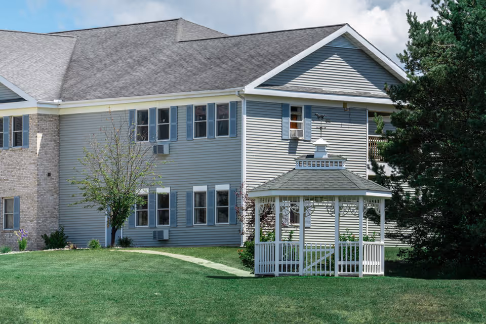 Two-story senior living building exterior with a white gazebo on a manicured lawn.