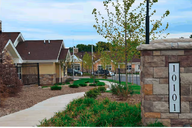 Landscaped sidewalk and planted beds leading past a stone address pillar marked 10101 toward residential buildings.