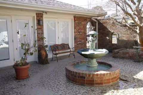 Outdoor courtyard with a brick fountain, bench, potted plants, and doors to residents' rooms.