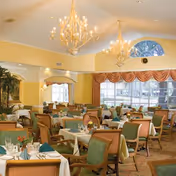 Bright dining room with multiple set tables, chandeliers, and large windows.