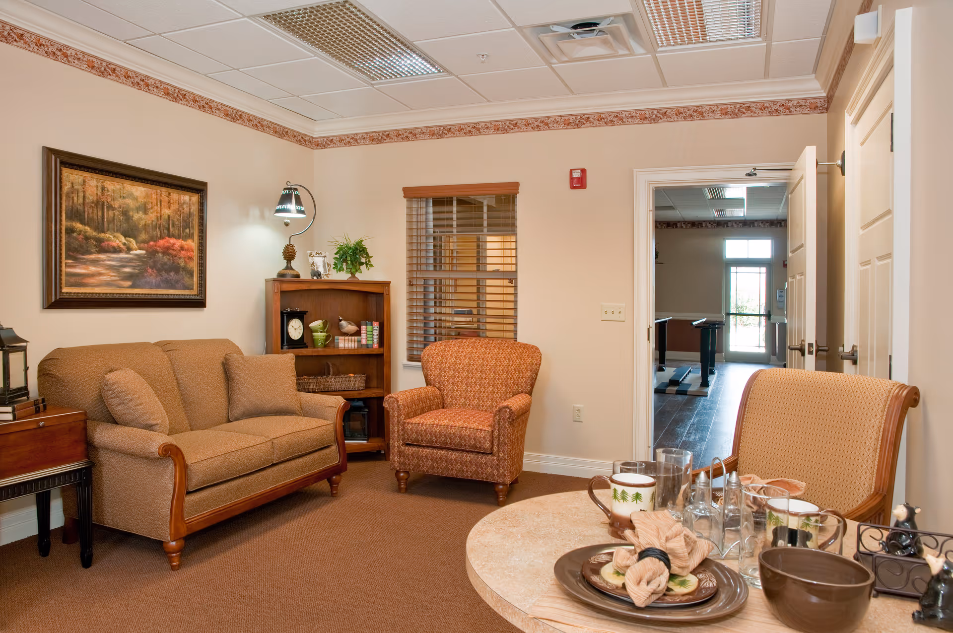 A comfortable living room with a sofa, two armchairs, a bookshelf, wall art, and a small table set with dishes.