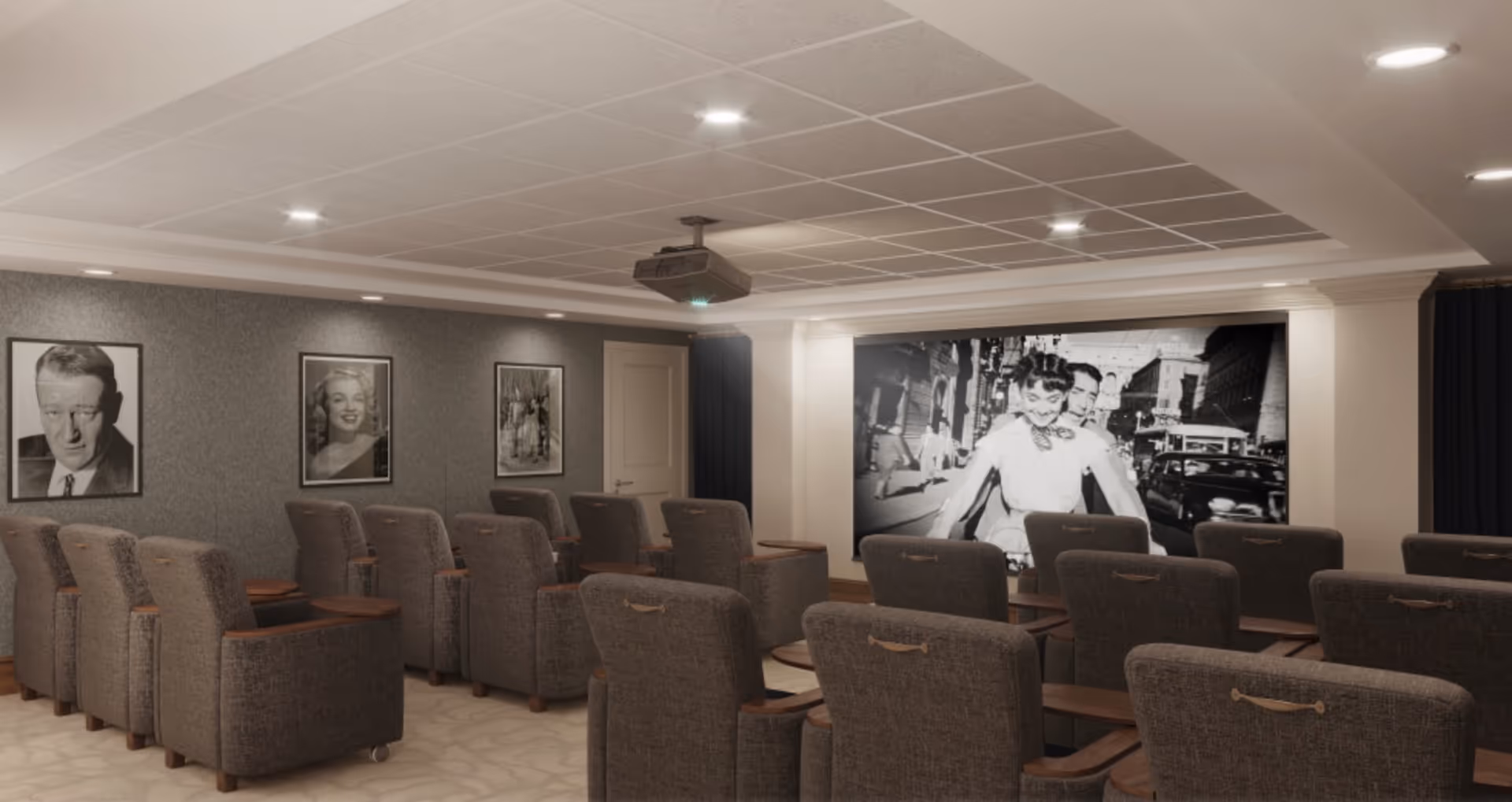A cozy screening room with rows of upholstered recliner seats facing a large projection screen showing a black-and-white film, framed portraits on the side wall, and a ceiling-mounted projector.
