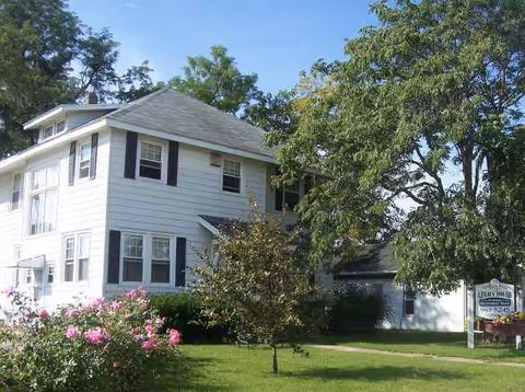 Exterior of Legacy House, a white two-story senior living facility with a lawn and blooming flowers.