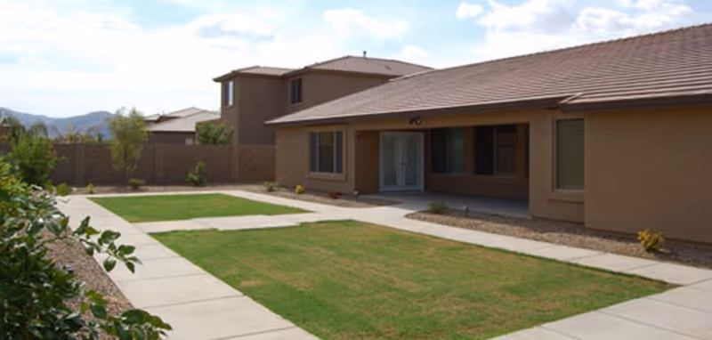 Single-story stucco building facing a central lawn with concrete walkways and a covered entrance.