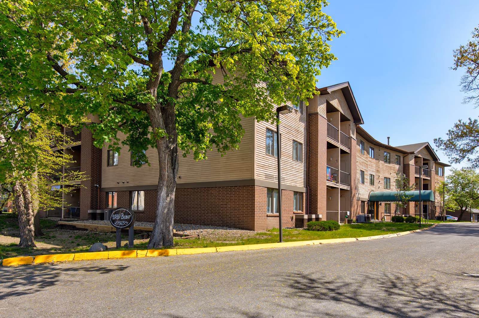 Three-story brick-and-siding senior apartment building with a green entrance awning, trees in front, and a driveway.