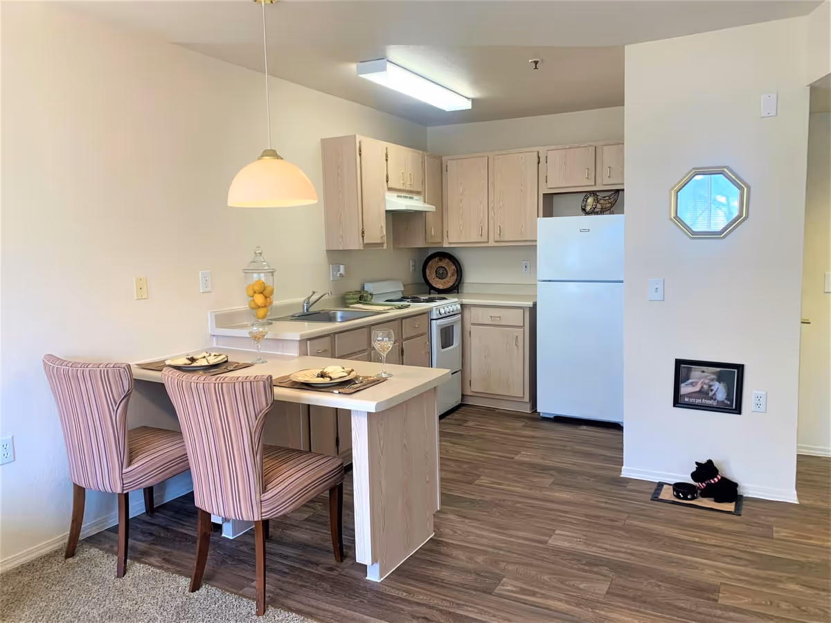 Small kitchen and dining nook with a breakfast bar, two striped chairs, light wood cabinets, and a refrigerator.