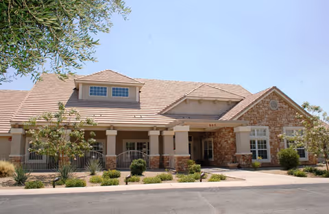 Single-story brick and stucco senior living facility with a covered entrance, landscaped front and a tiled roof under a clear sky.