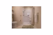 Accessible bathroom with a shower/tub combo, shower curtain, toilet, grab bars, towel rack, and a bath mat.