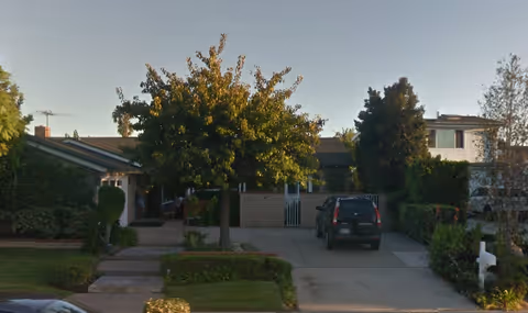 Single-story house front with a central tree, driveway, and an SUV parked in front.