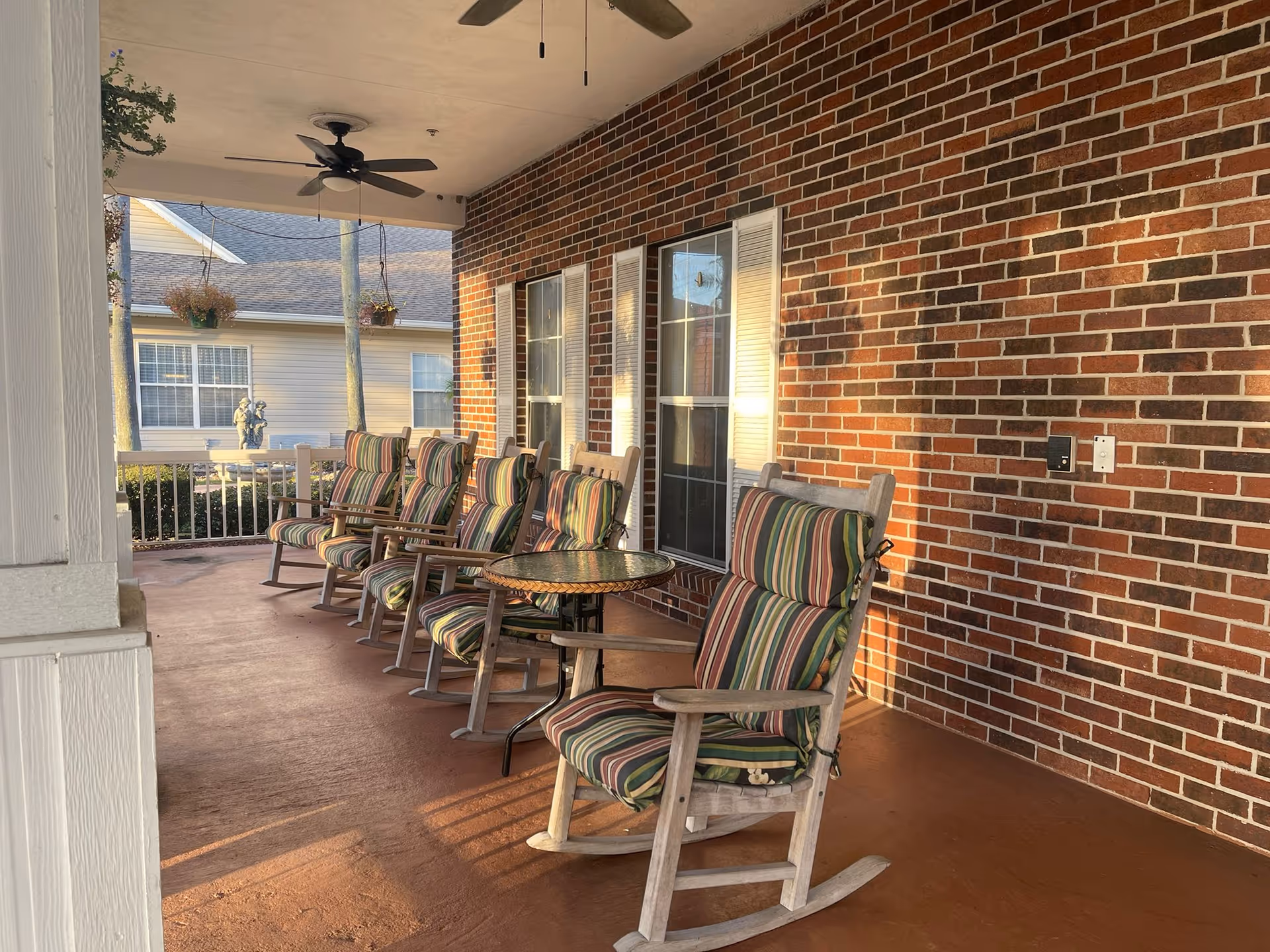 Covered brick-front porch with a row of cushioned striped rocking chairs and a small round table.