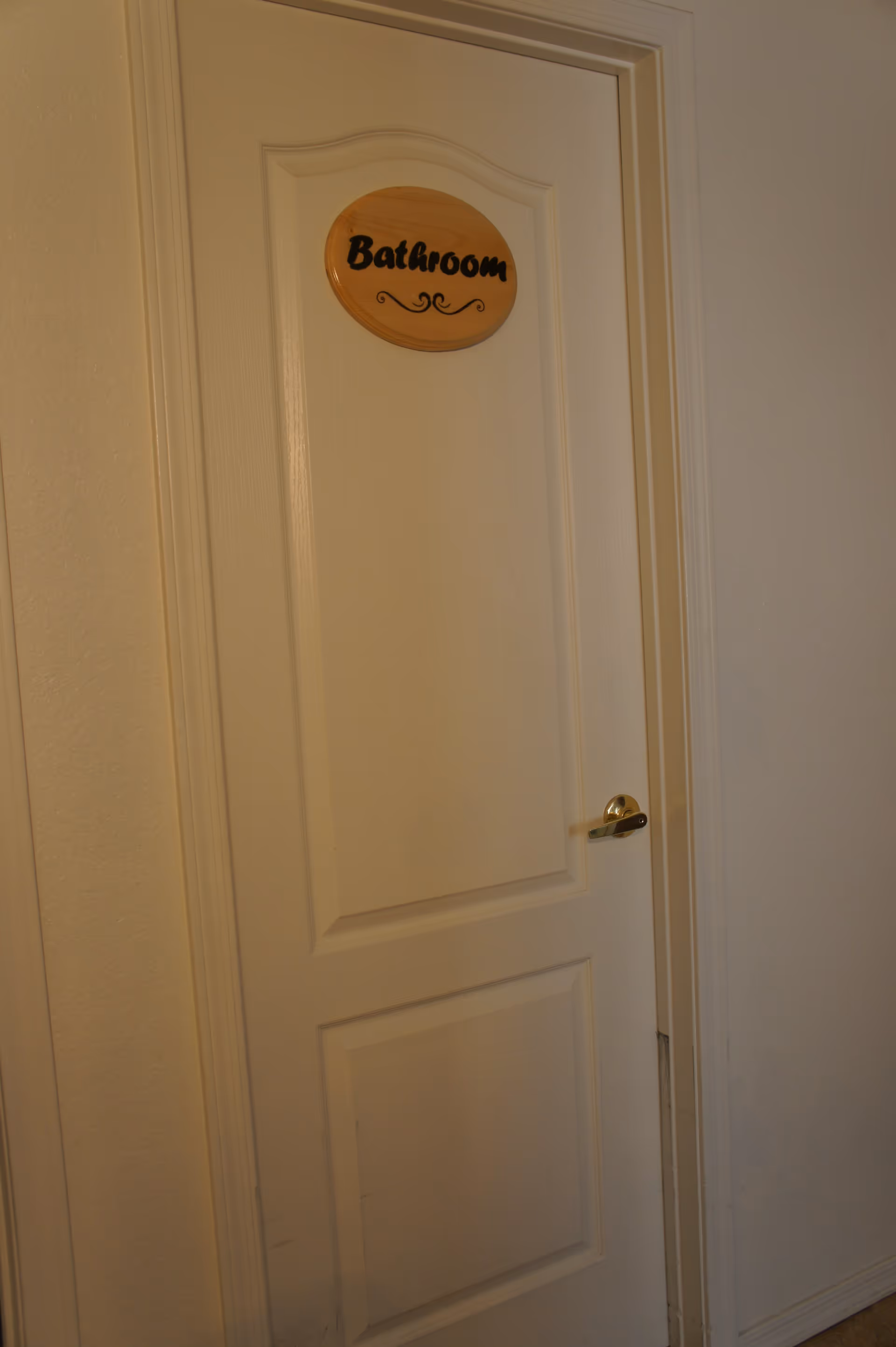 Closed white paneled door with a wooden 'Bathroom' sign and a silver handle.