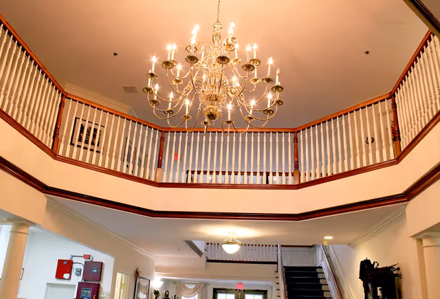 Interior lobby featuring a large ornate chandelier, a second-floor balcony with white railings, and a staircase leading up.