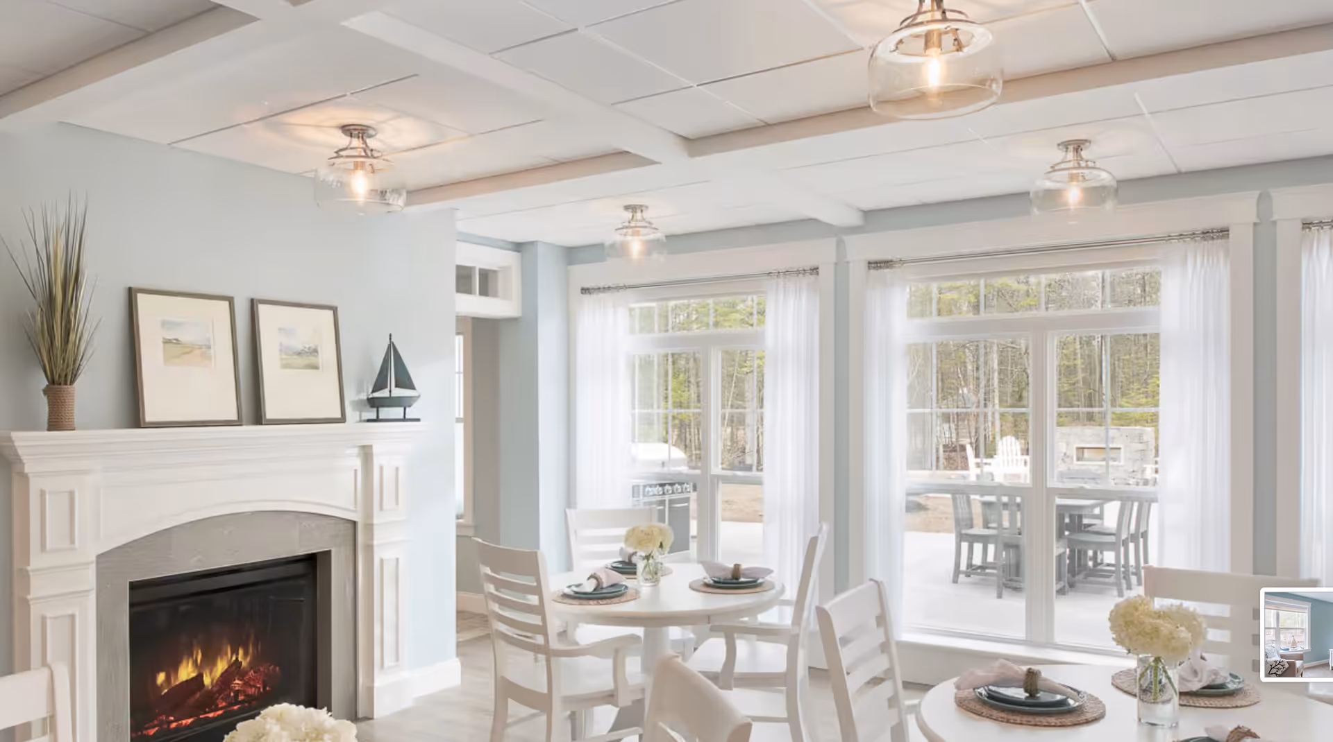 Bright dining area with round tables and chairs, a fireplace, and large windows overlooking an outdoor patio.