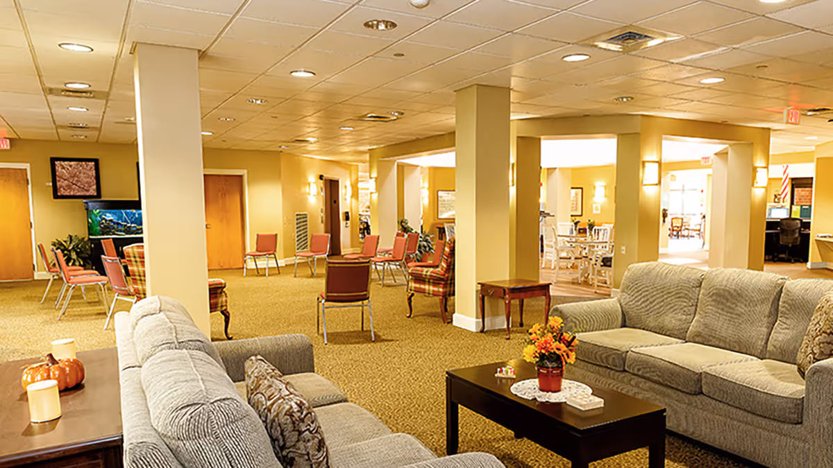 Bright, spacious senior living common room with sofas, chairs, coffee tables and warm lighting.