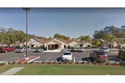Exterior view of a single-story senior living facility with parking lot and palm trees.