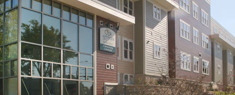 Front exterior of Oak Park Place Nakoma senior living building with large windows and a sign.
