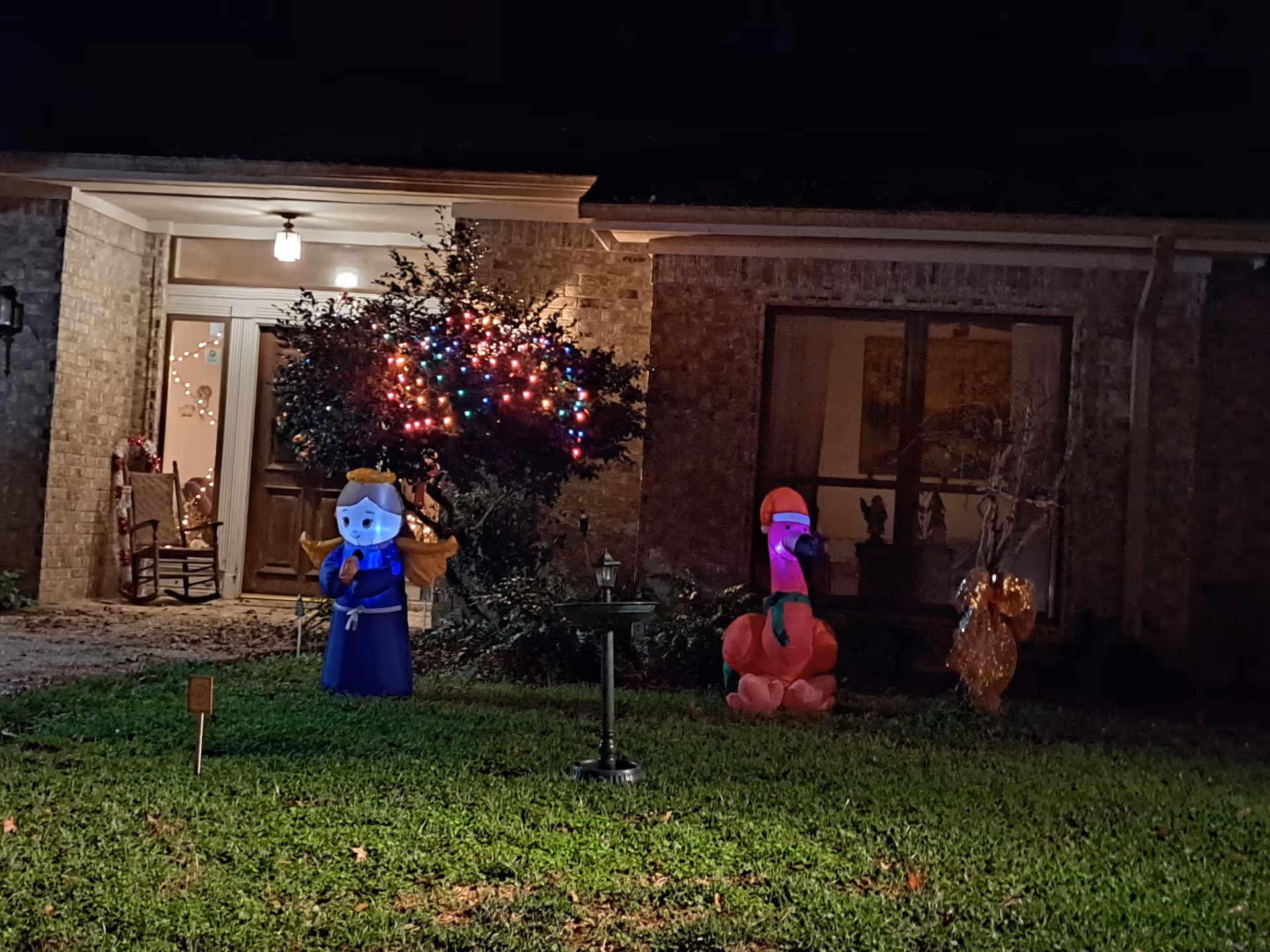 Night view of a brick house front yard decorated with a tree of multicolored lights and inflatable holiday figures on the lawn.