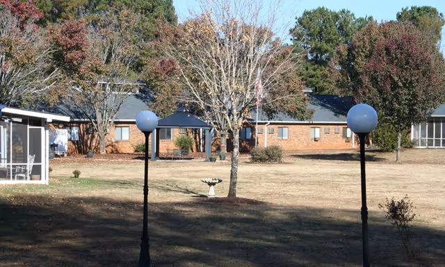 Courtyard lawn with two lamp posts, a birdbath, trees and a low brick senior living building in the background.