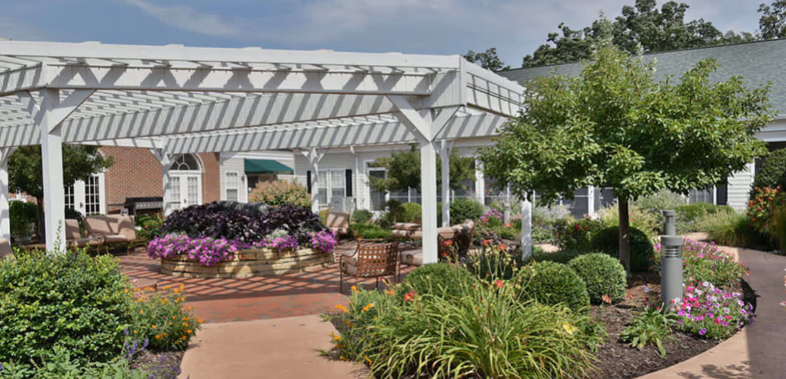 Outdoor courtyard with a white pergola, central flowerbed, seating areas, and landscaped pathways.