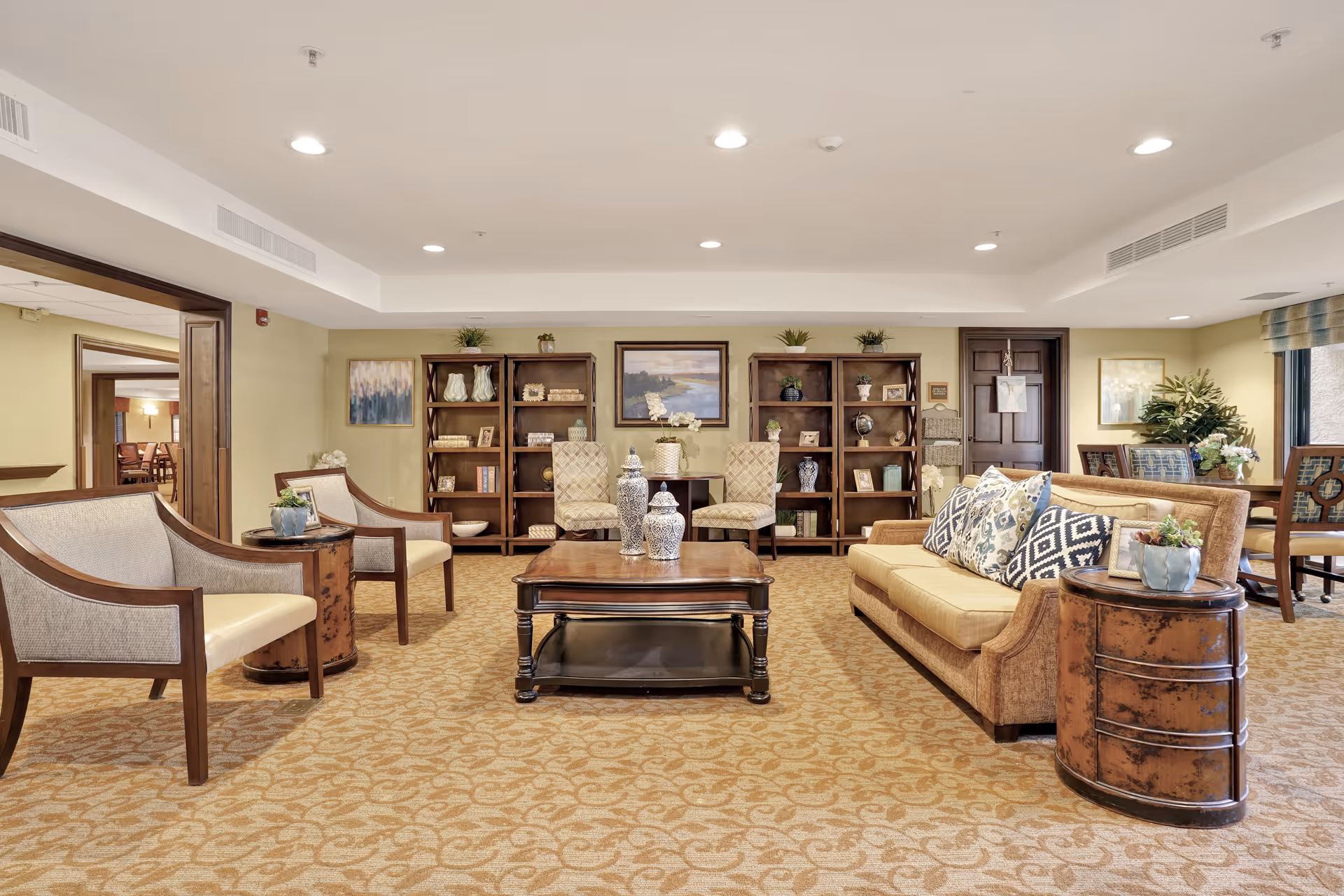 Bright furnished common lounge with sofas, armchairs, a coffee table, and bookshelves.