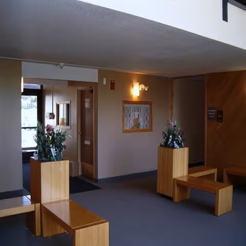 Lobby-style interior with wooden benches, planter boxes, wall art, and a hallway entrance.