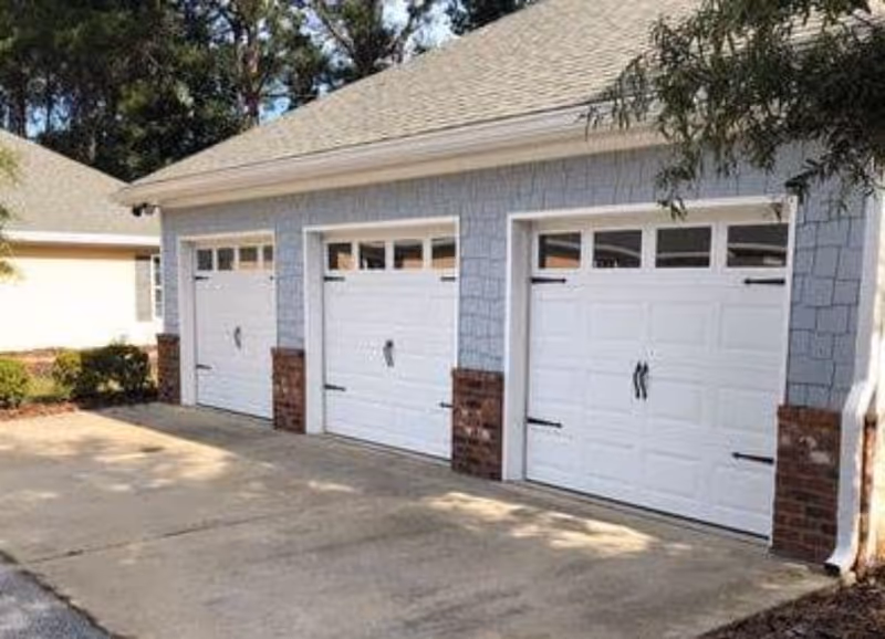 Exterior view of a light blue building with three white garage doors and brick accents.