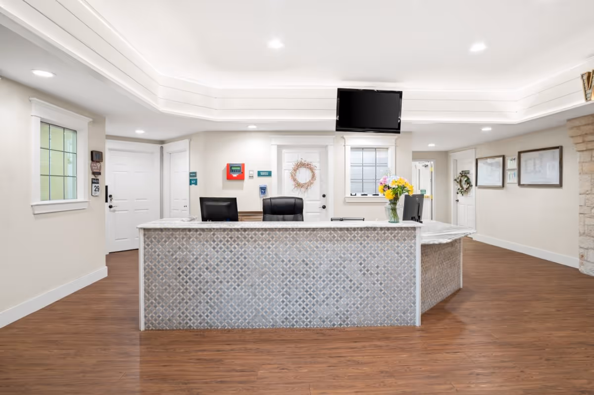 Reception desk and lobby area with a patterned front counter, two chairs, wall TV, and a vase of flowers.