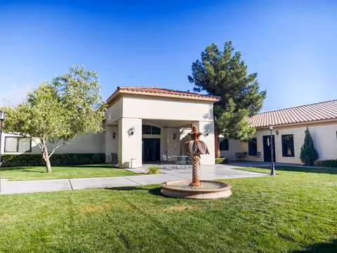 Front view of a senior living facility with a courtyard lawn and fountain statue.