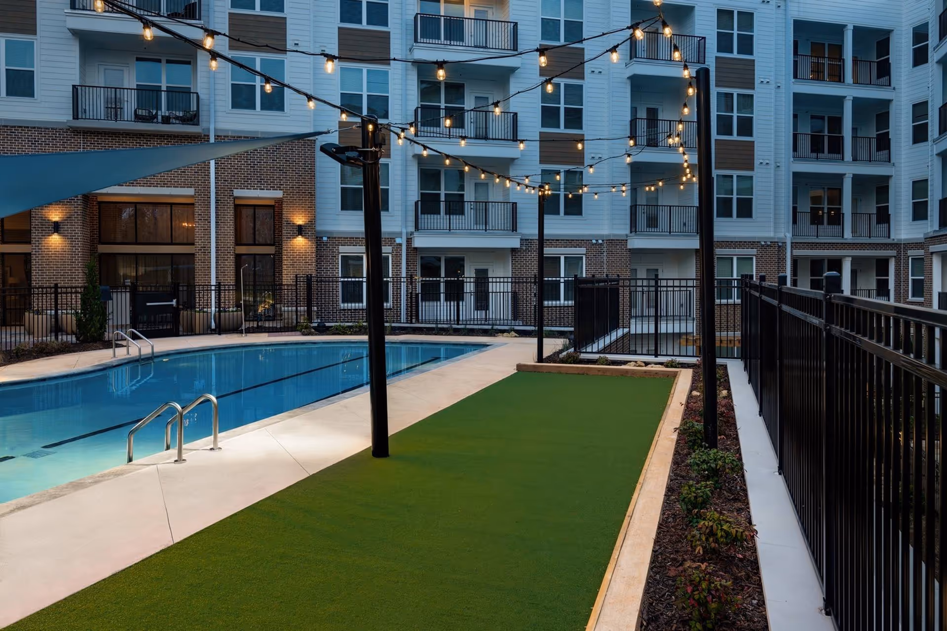 Courtyard pool area with string lights, a putting-green style lawn and surrounding multi-story apartment balconies.