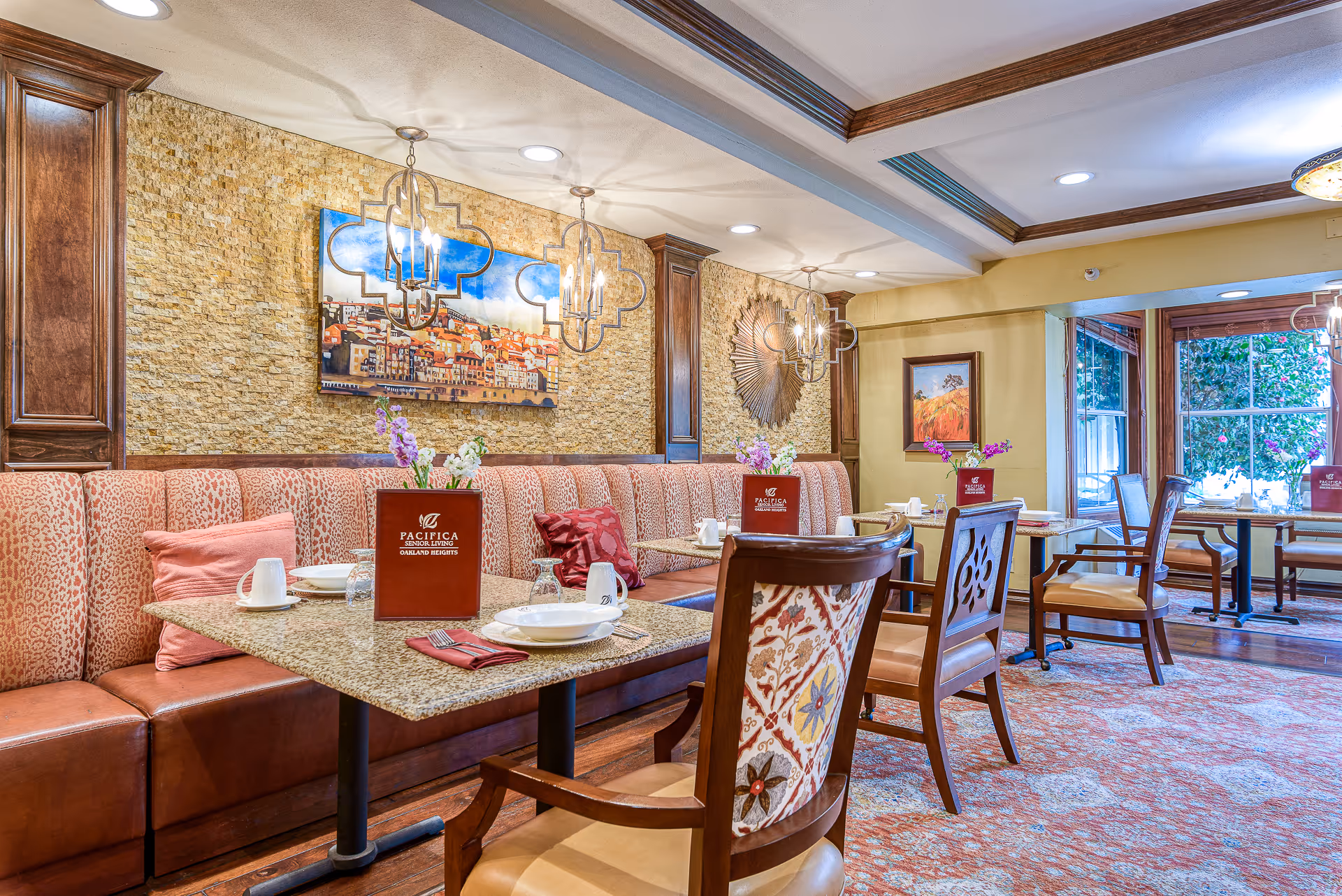 Elegant dining room with upholstered banquette seating, set tables and wooden chairs beneath decorative pendant lights and artwork.