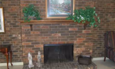 Brick fireplace with framed painting, two mantel plants, and seating in a cozy living room.