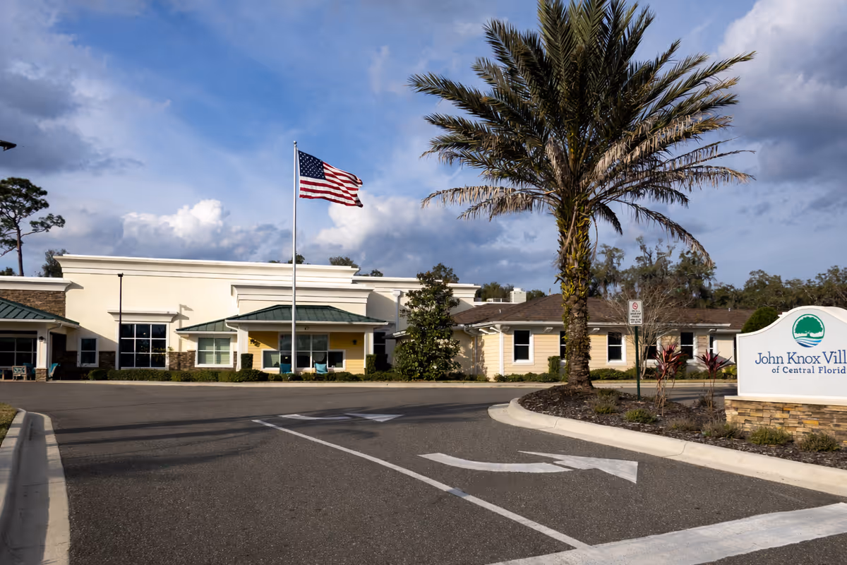 Exterior view of a senior living facility with a flagpole and palm tree.