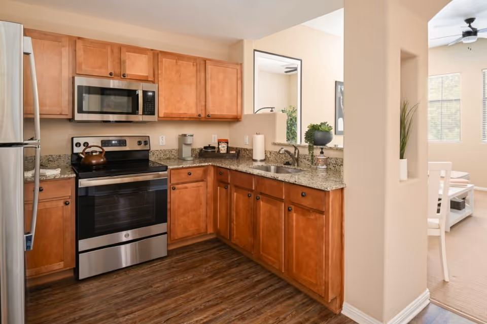Open kitchen with wooden cabinets, granite countertops, stainless steel appliances, and a pass-through to the dining area.