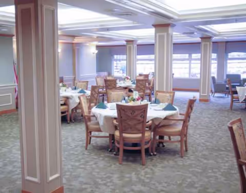 Spacious dining room in a senior living facility with round tables and purple accents.