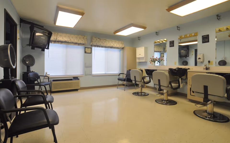 An interior hair salon with styling chairs, mirrors, shampoo sinks and waiting chairs in a senior living facility.