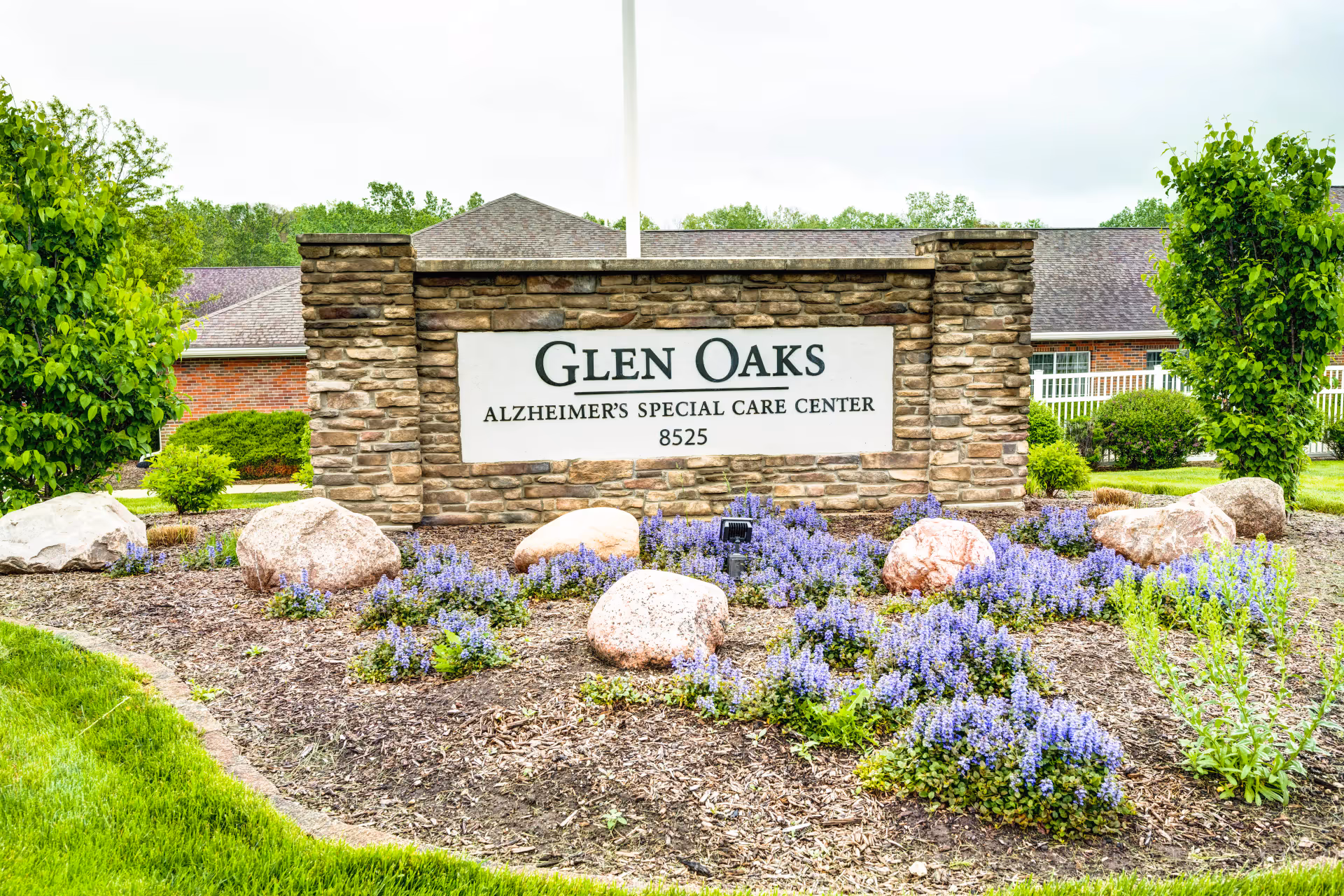 Stone entrance sign for Glen Oaks Alzheimer's Special Care Center surrounded by landscaping and purple flowers.
